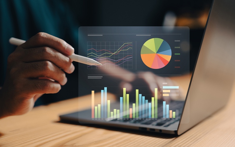 a hologram of metrics and data charts hovering over a laptop on a desk - Credit: iStock - ipuwadol - 1699670758